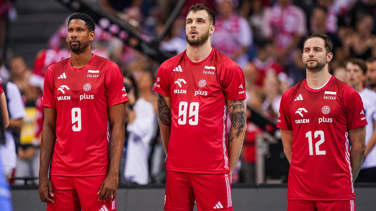 Trzech siatkarzy w czerwonych strojach reprezentacji Polski na tle trybun.