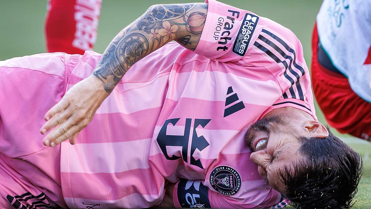 Piłkarz Lionel Messi w różowej koszulce na boisku, trzymający się za rękę i wyglądający na cierpiącego z powodu kontuzji.