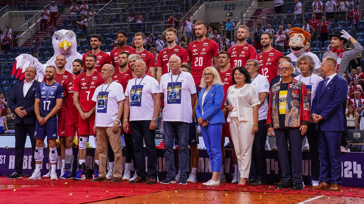 Drużyna siatkarzy w strojach reprezentacyjnych podczas Memoriału Wagnera, stojąca na podium z pucharem, z maskotką i osobami z sztabu.