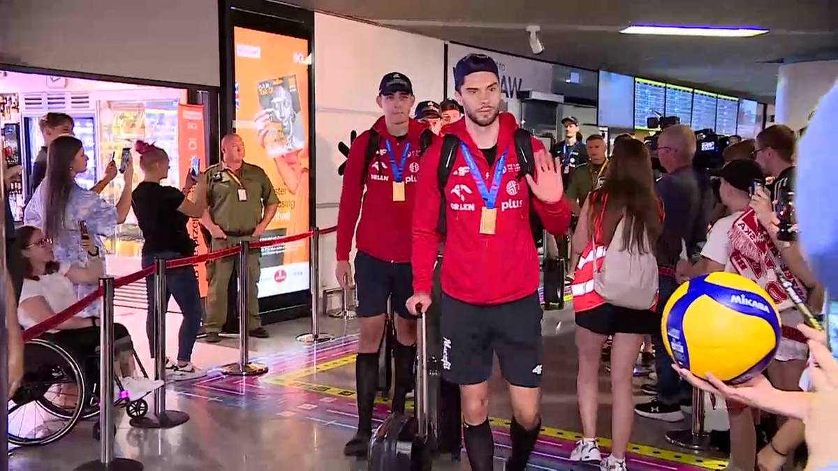 Dw&oacute;ch młodych mężczyzn w czerwonych bluzach z kapturem i medalach na szyi, idzie z plecakami. Przed nimi stoi osoba w&oacute;zku inwalidzkim.