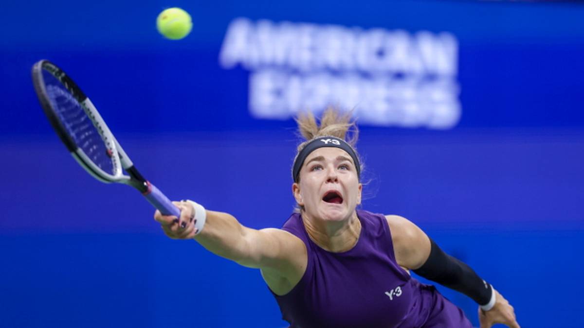 Tenisistka z rozchyloną w krzyku twarzą i wyciągniętą ręką z rakietą, uderza piłkę w locie.