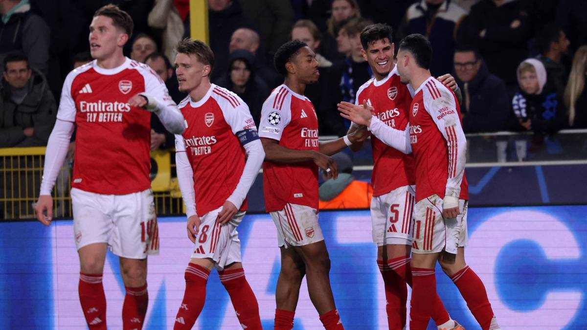 Pięciu piłkarzy w czerwono-białych strojach piłkarskich świętuje na boisku.