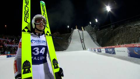 Skoczek narciarski w białym kombinezonie z neonowożółtymi nartami marki Fischer, przygotowuje się do skoku na skoczni narciarskiej w Falun. Widoczny numer 34 na nartach.