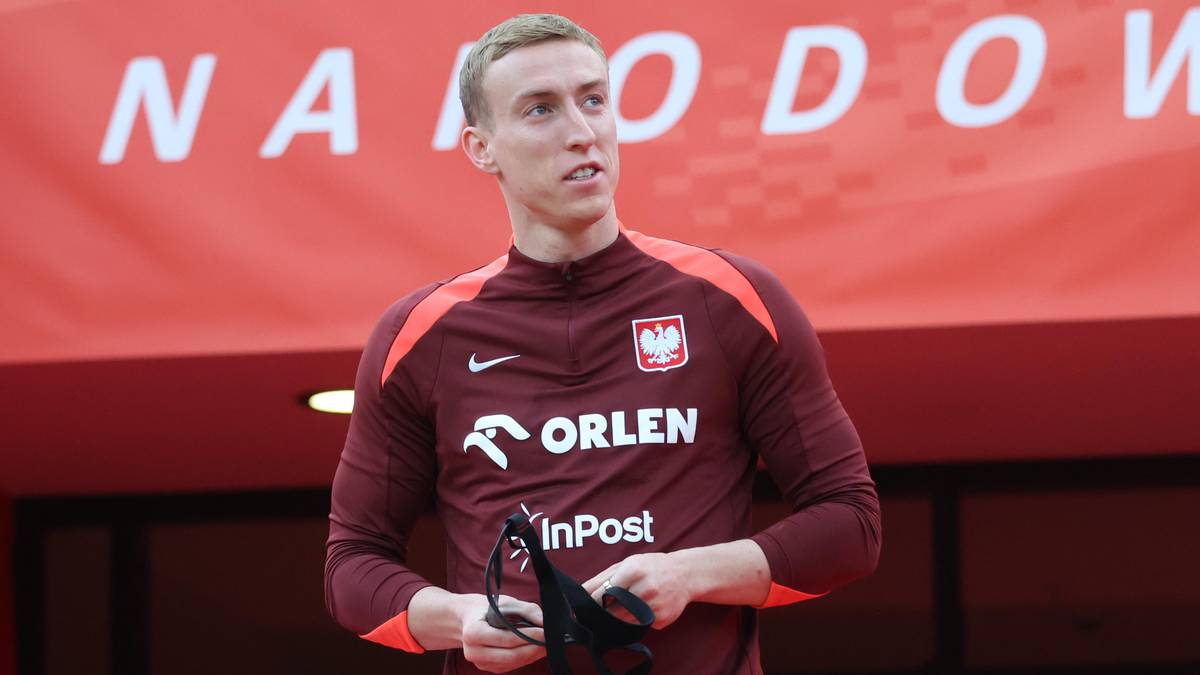 Piłkarz w bordowej koszulce reprezentacji Polski z orłem na piersi, stojący przed napisem PGE Narodowy.