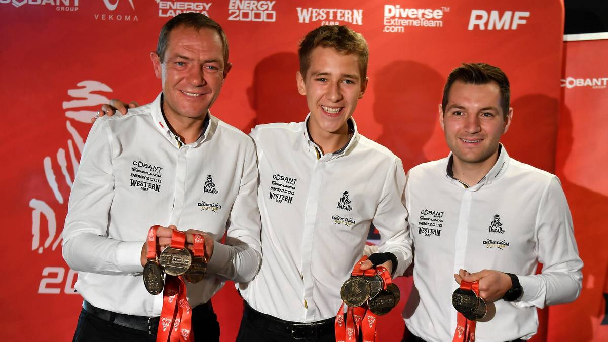 Trzech mężczyzn w białych koszulkach zespołu Energylandia Rally Team prezentuje medale.