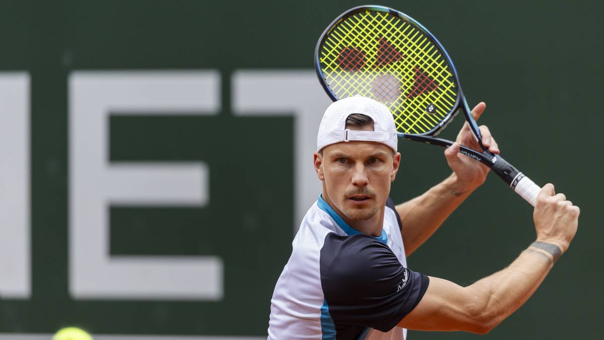 Mężczyzna w białej czapce i koszulce tenisowej, trzymający rakietę tenisową, przygotowuje się do uderzenia.