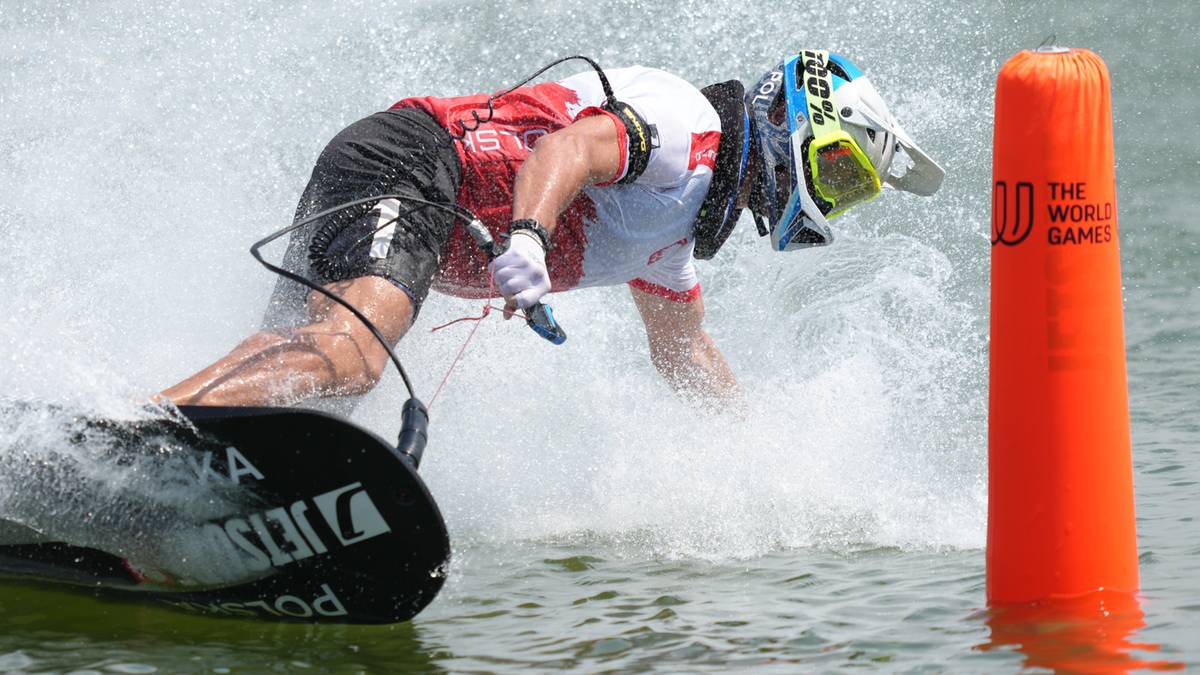 Zawodnik na skuterze wodnym wykonuje zwrot, rozpryskując wodę. Zawodnik ma na sobie kask i specjalistyczny strój.