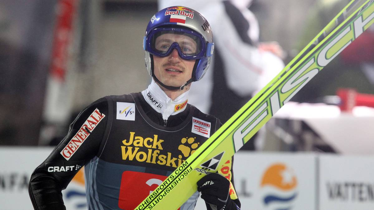 Adam Małysz, polski skoczek narciarski, w kombinezonie i kasku trzymający narty.