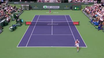 Kort tenisowy z dwoma zawodnikami w akcji, otoczony trybunami pełnymi widz&oacute;w. Na siatce widoczne logo ATP Tour.