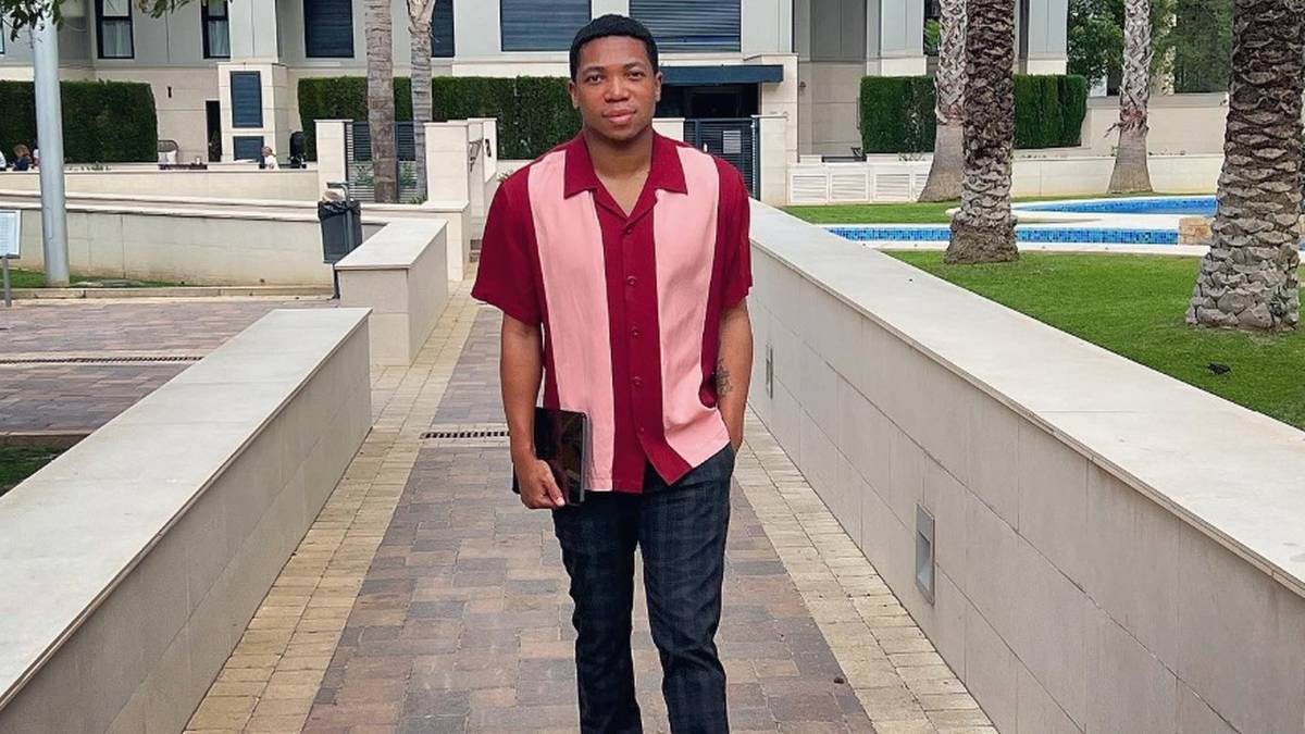 Młody mężczyzna idzie po chodniku w stronę widza, ubrany w dwukolorową koszulę i ciemne spodnie.