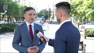 Mężczyzna w garniturze odpowiada na pytania dziennikarza trzymającego mikrofon.