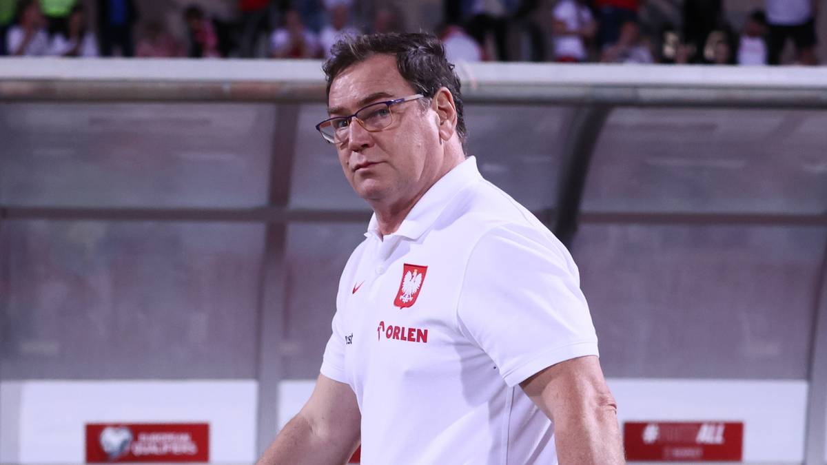 Trener Jan Urban w koszulce reprezentacji Polski idzie po bieżni stadionu.