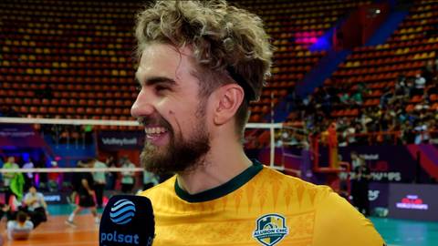 Portret siatkarza Jakuba Popiwczaka w ż&oacute;łtej koszulce, uśmiechniętego, z mikrofonem Polsatu przed nim.