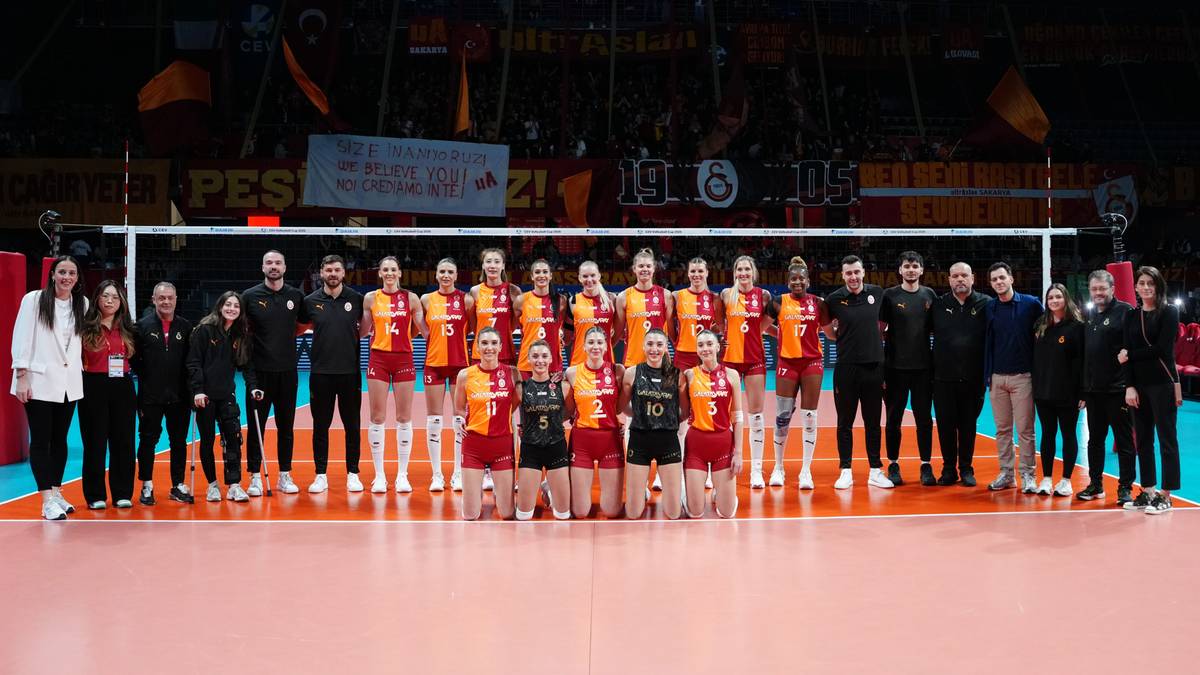 Dwie drużyny siatkarskie pozujące do zdjęcia na boisku przed meczem, z publicznością na trybunach w tle.