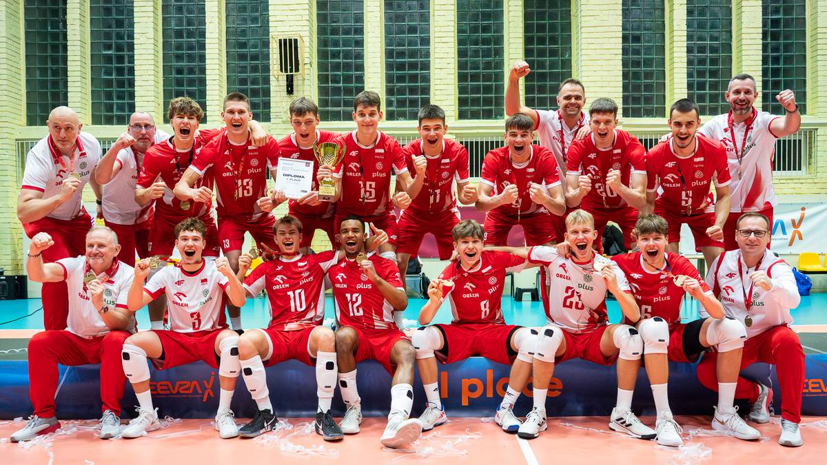 Drużyna siatkarska mężczyzn poniżej 18 roku życia w czerwonych strojach pozuje do wspólnego zdjęcia z pucharem, większość zawodników siedzi w pierwszym rzędzie.