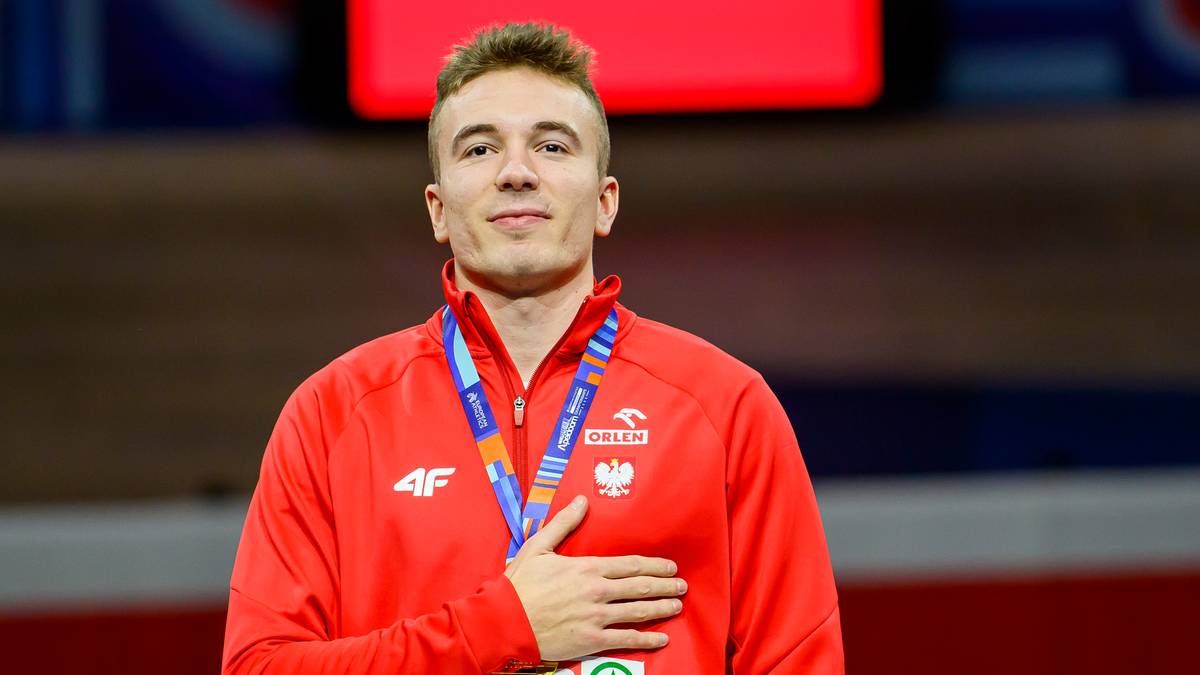 Sportowiec w czerwonej bluzie z medalem na szyi, trzymający się za serce.