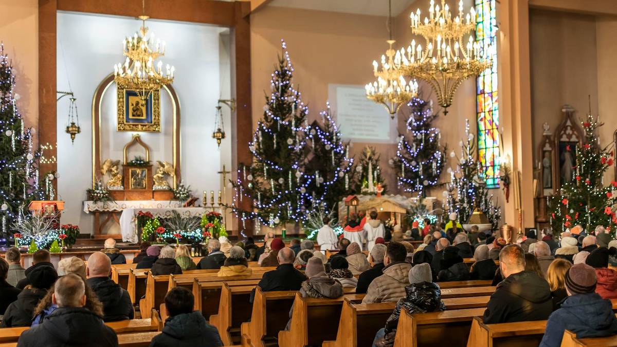 Wnętrze kościoła podczas uroczystości, z wiernymi w ławkach, ozdobionymi choinkami i ołtarzem.