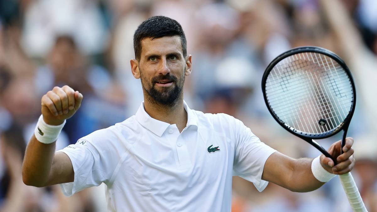 Novak Djokovic świętuje zwycięstwo, trzymając rakietę tenisową i zaciśniętą pięść. Ma na sobie białą koszulkę polo z logo Lacoste.