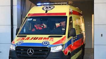 Karetka pogotowia ratunkowego z włączonymi sygnałami świetlnymi wyjeżdża z garażu.