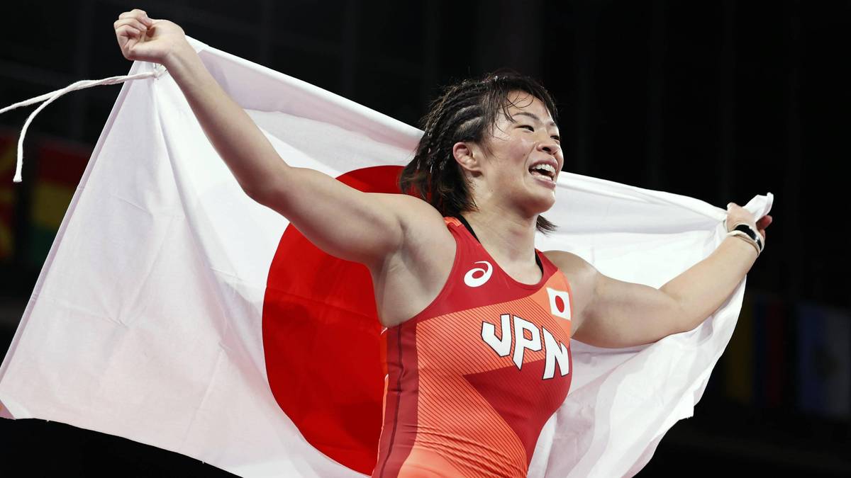 Mistrzyni olimpijska w zapasach, zapaśniczka z Japonii, unosi flagę Japonii z wyrazem triumfu na twarzy.