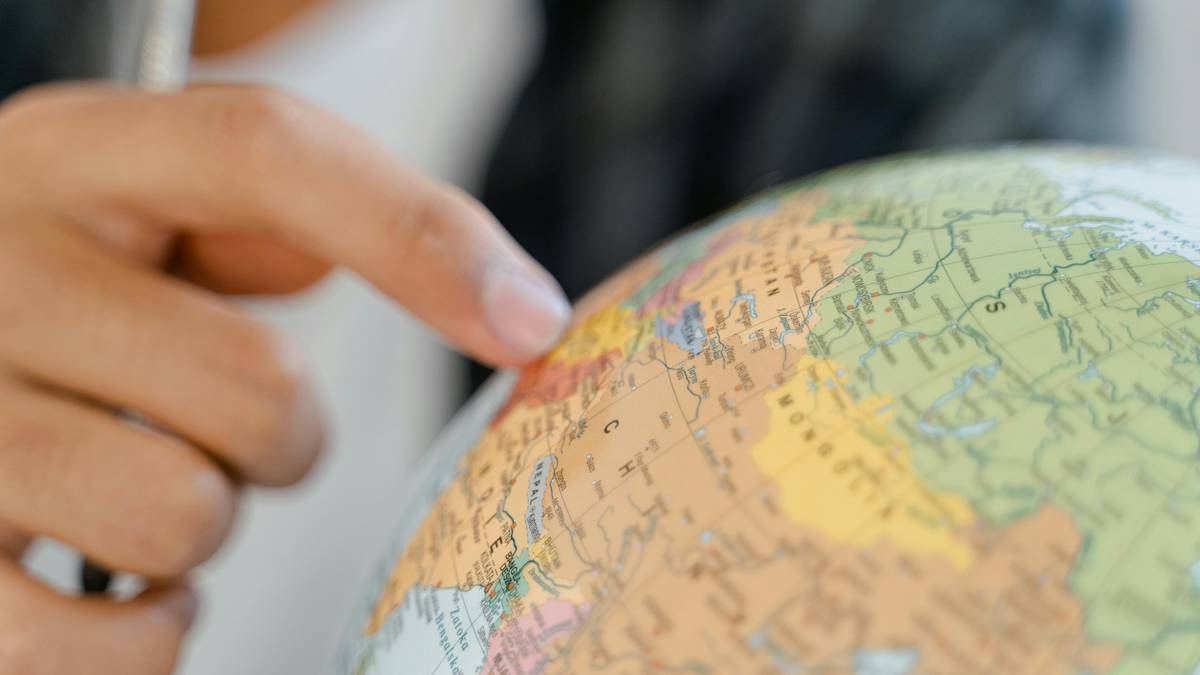 Dłoń wskazująca palcem na mapę świata na globusie, widoczna część Europy i Azji.