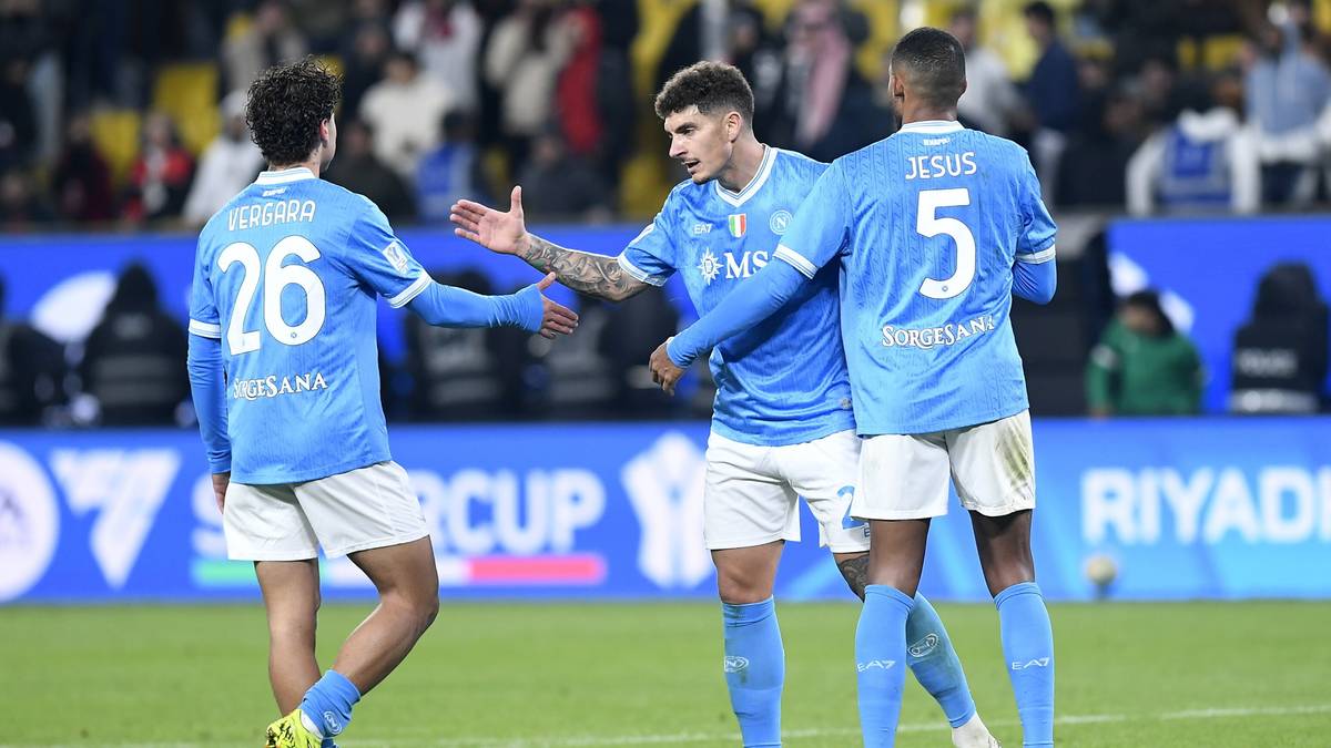 Trzech piłkarzy w niebieskich strojach celebruje zdobycie bramki na boisku.