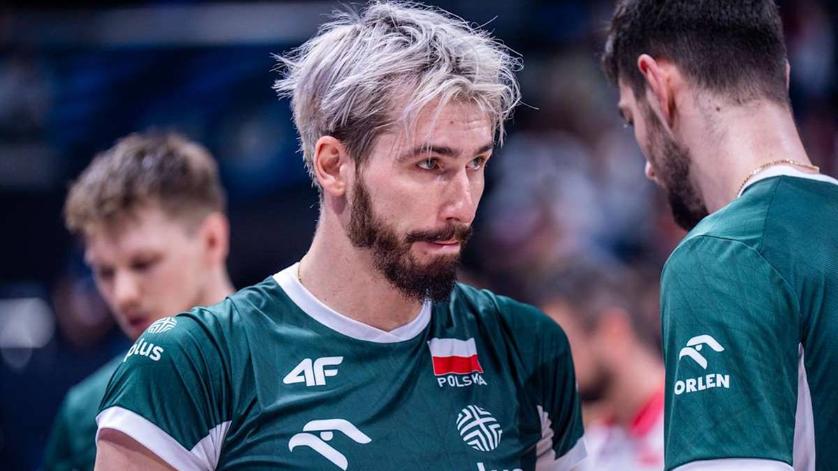 Siatkarz reprezentacji Polski z krótką, blond fryzurą i brodą, ubrany w zieloną koszulkę, rozmawia z innym zawodnikiem.