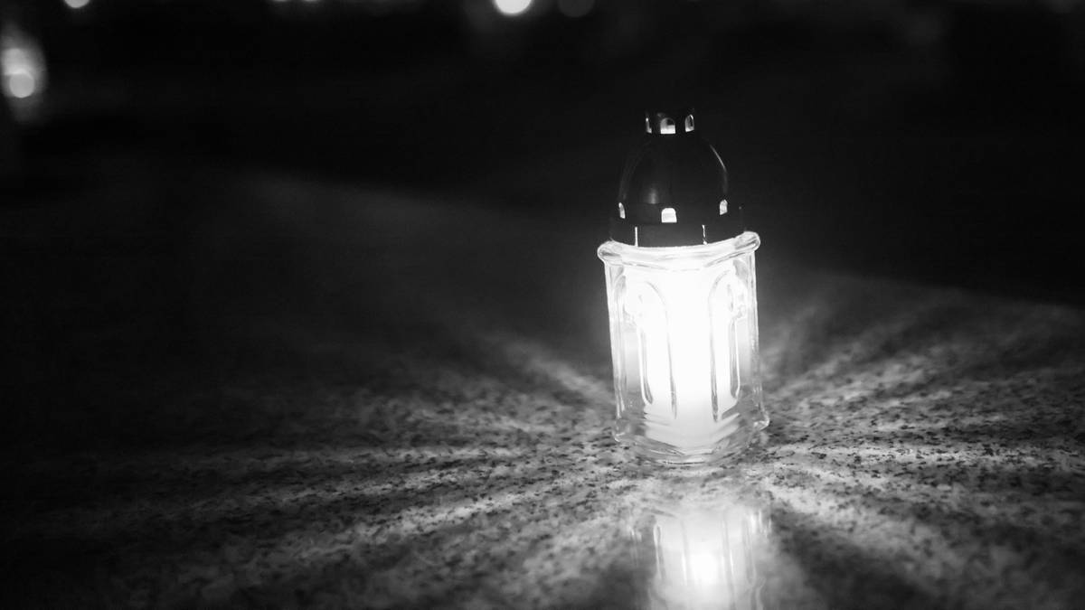 Płonąca świeca cmentarna na kamiennym nagrobku, nocą. Blask świecy rozprasza się na kamieniu.