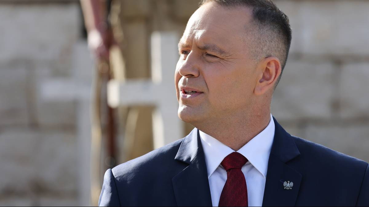 Portret mężczyzny w garniturze i krawacie, patrzącego w bok. W tle niewyraźna postać i biały krzyż.