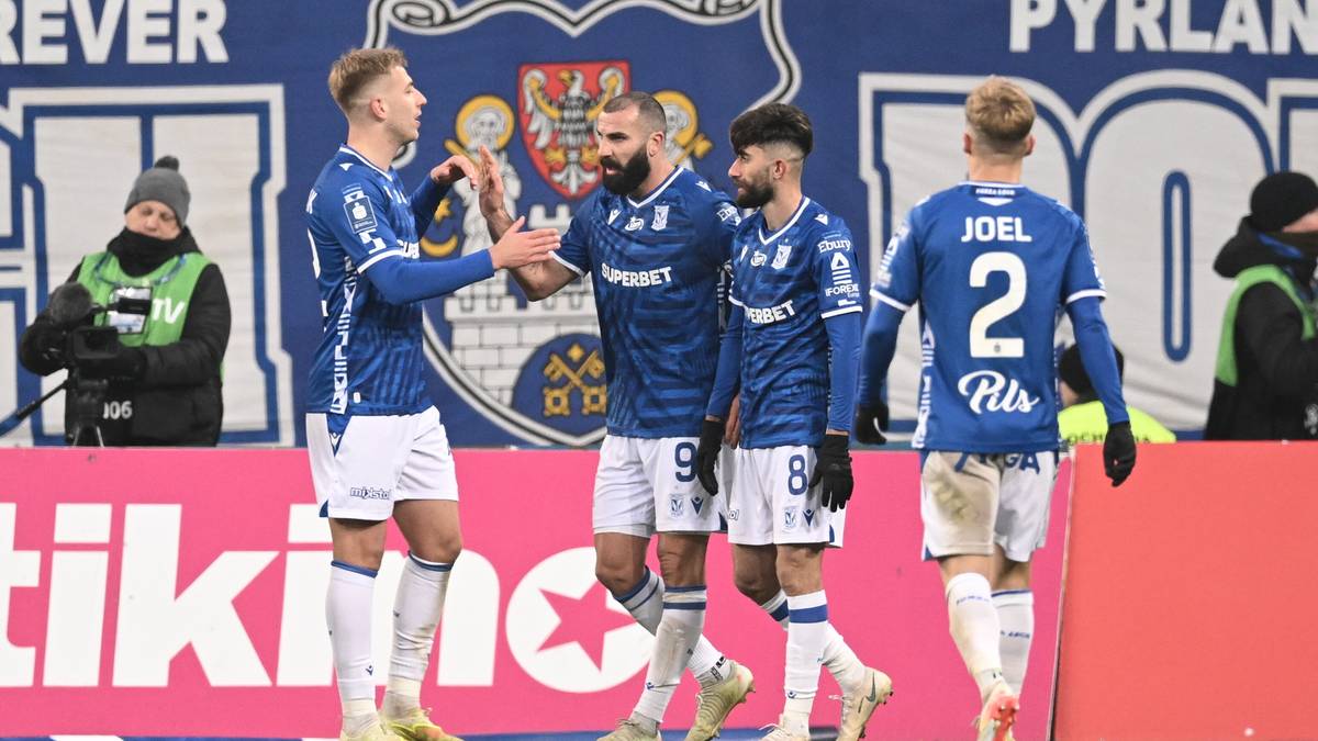 Piłkarze Lecha Poznań w niebieskich strojach świętują zdobytego gola, dwóch z nich jest blisko siebie, jeden z nich podnosi rękę w geście radości.