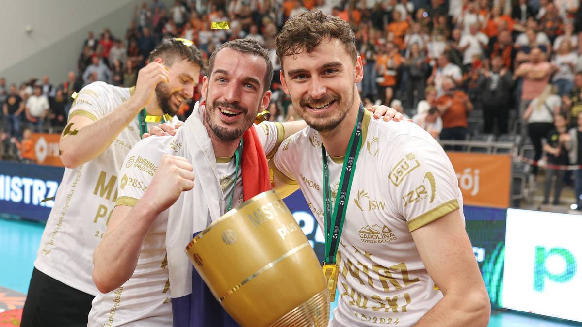 Dwóch siatkarzy Jastrzębskiego Węgla świętuje z pucharem, w tle trybuny z kibicami.