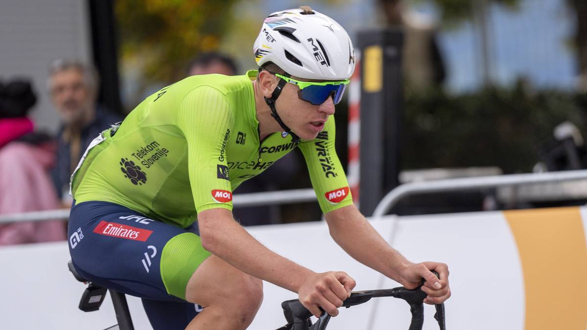Kolarz Tadej Pogacar w zielonej koszulce i niebieskich spodenkach z numerem startowym jedzie na rowerze w pozycji czasowej.