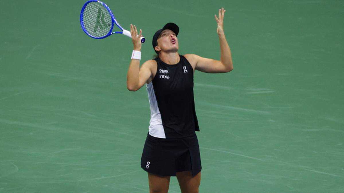 Iga Świątek po zwycięskim meczu wznosi ręce w górę w geście radości, trzymając rakietę tenisową w lewej ręce.