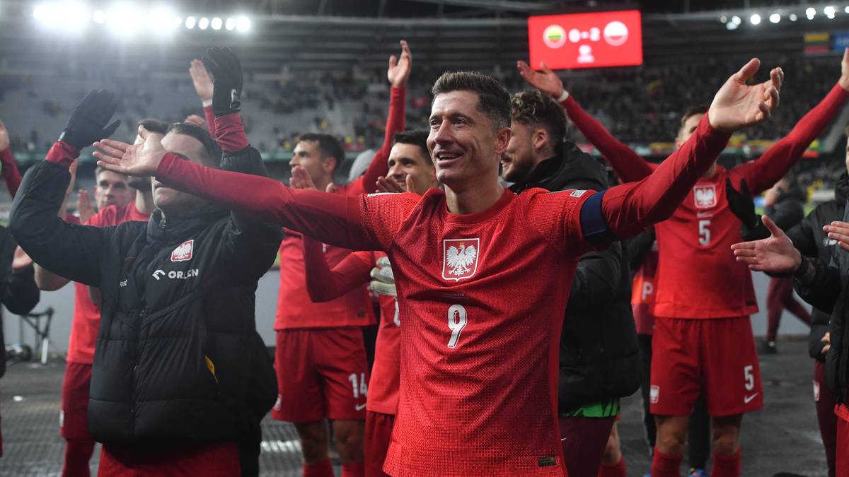 Piłkarz Robert Lewandowski w koszulce reprezentacji Polski z numerem 9, na tle kolegów z drużyny świętujących sukces na boisku.