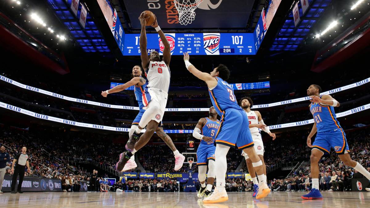 Dwóch zawodników w białych strojach próbujących zatrzymać gracza w niebieskim stroju podczas meczu koszykówki NBA.