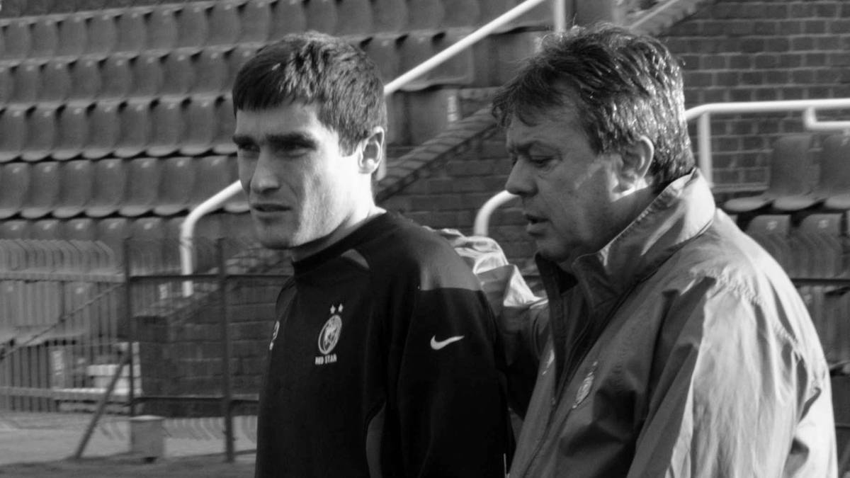 Dw&oacute;ch mężczyzn, prawdopodobnie trener i piłkarz, idzie po boisku piłkarskim.