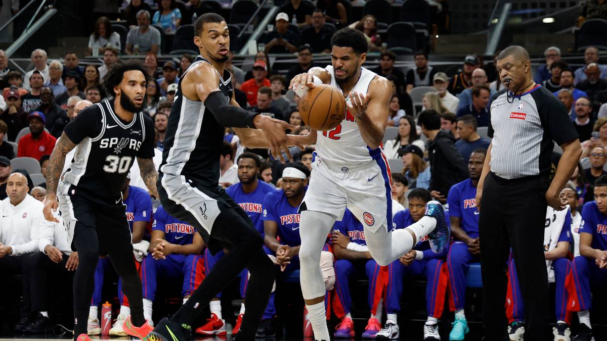 Gracz w białym stroju z piłką w rękach, otoczony przez przeciwnik&oacute;w podczas meczu koszyk&oacute;wki.