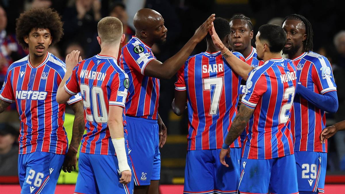 Drużyna piłkarska Crystal Palace w swoich strojach sportowych świętuje zwycięstwo na boisku, z publicznością na trybunach w tle.