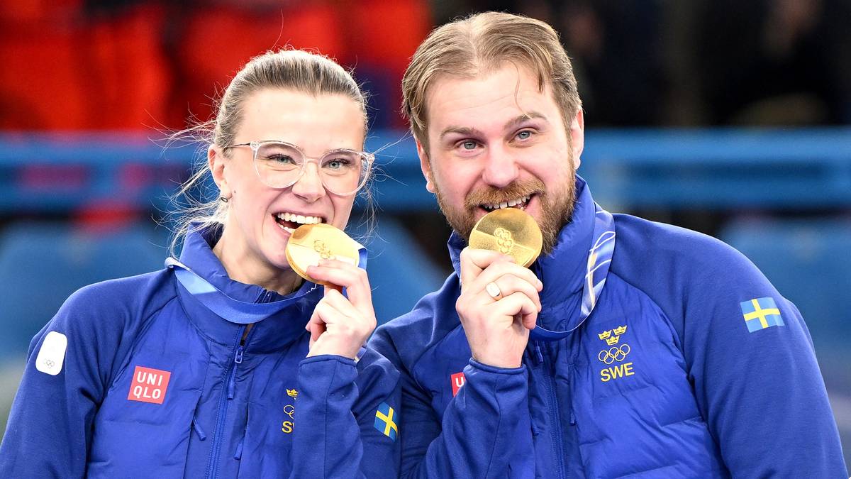 Para sportowc&oacute;w w niebieskich kurtkach z medalem na szyi, uśmiechają się.