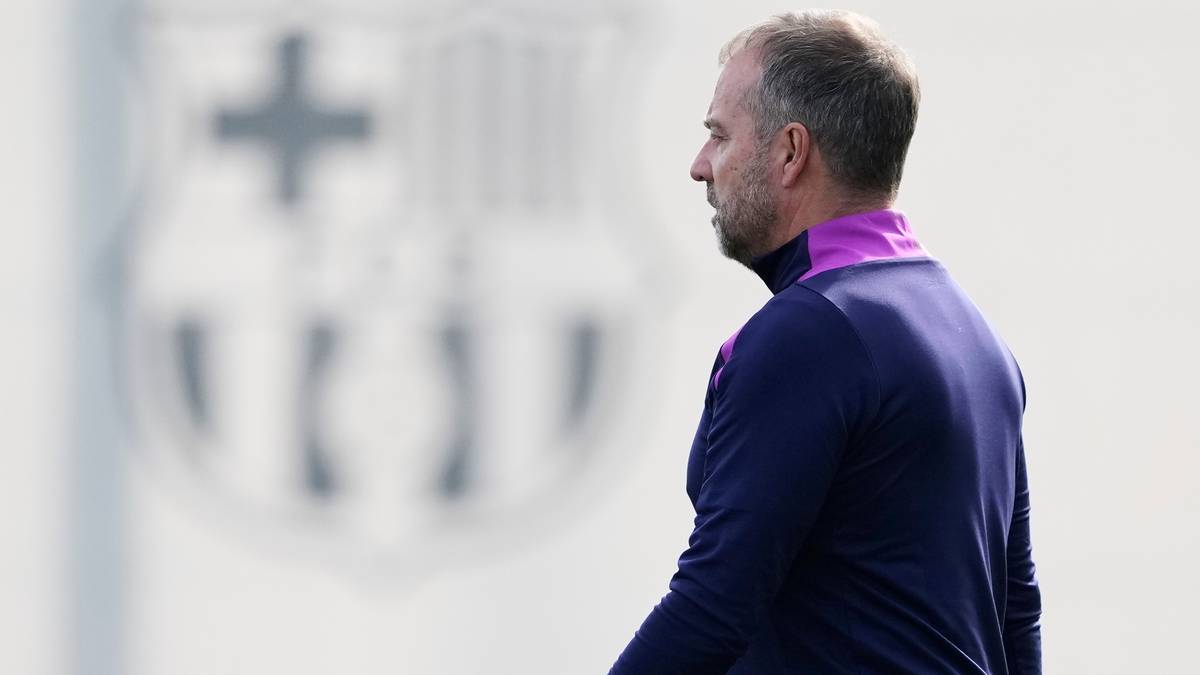 Mężczyzna w granatowej bluzie z fioletowym kołnierzem, w profilu, na tle rozmytego herbu FC Barcelona.