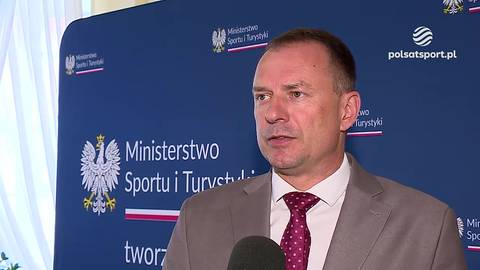 Piotr Borys, polityk, stoi przed tablicą Ministerstwa Sportu i Turystyki i przemawia do mikrofonu.