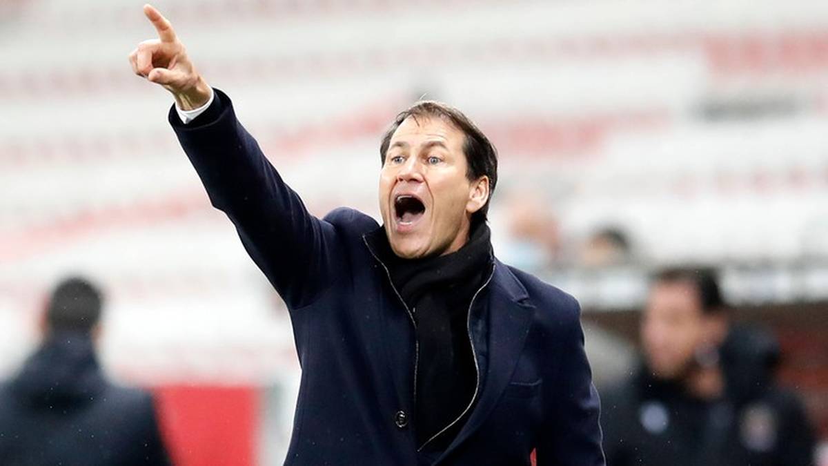 Trener w niebieskiej kurtce i czarnym szaliku wskazuje palcem w g&oacute;rę, krzycząc.