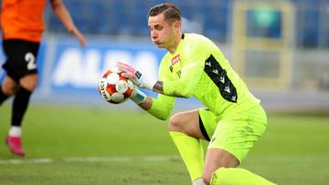 Bramkarz w ż&oacute;łtym stroju bramkarskim trzyma piłkę w rękach.