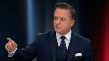 Bogdan Rymanowski w garniturze gestykuje podczas prowadzenia programu