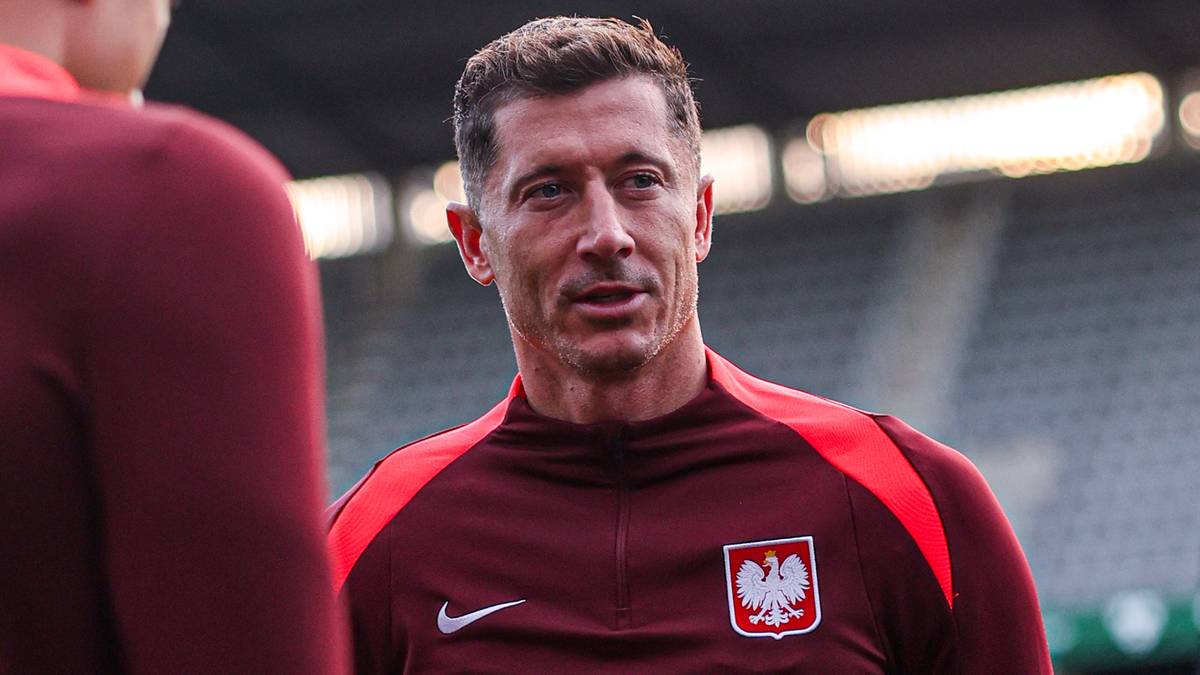 Robert Lewandowski w nowej koszulce reprezentacji Polski, stojący w otoczeniu koleg&oacute;w z drużyny na stadionie.