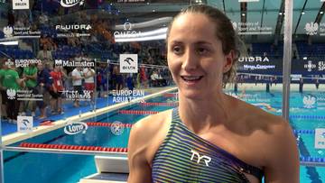 Katarzyna Wasick, uśmiechnięta pływaczka w stroju TYR, udziela wywiadu na tle basenu pływackiego.