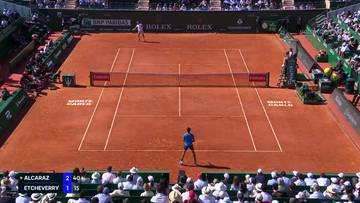 Kort tenisowy z glinianą nawierzchnią, na którym rozgrywany jest mecz między Carlosem Alcarazem a Tomasem Martinem Etcheverrym. Na dole ekranu widoczna jest tablica wyników.