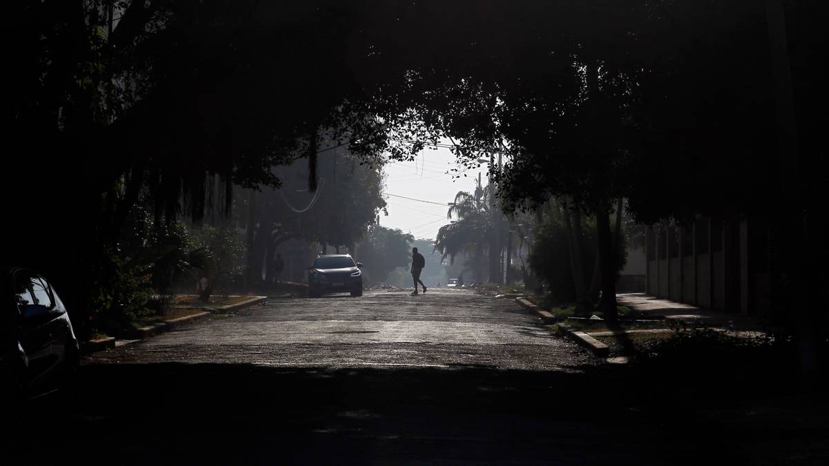 Mroczna ulica z drzewami po bokach, na środku ulicy stoi samoch&oacute;d, a w oddali idzie samotna postać.
