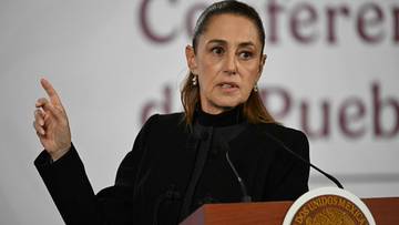 Kobieta w czarnym żakiecie przemawia przy m&oacute;wnicy, gestykulując prawą ręką.