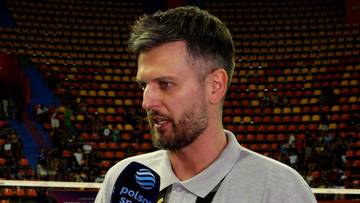 Portret Michała Winiarskiego, siatkarza, z brodą i kr&oacute;tkimi włosami, m&oacute;wiącego do mikrofonu z logo Polsat Sport. W tle widać trybuny wypełnione widzami.